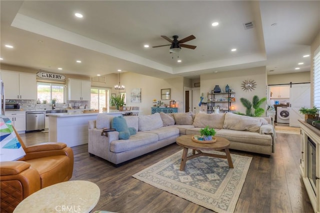 living room with washer / clothes dryer, visible vents, dark wood-style floors, a tray ceiling, and recessed lighting