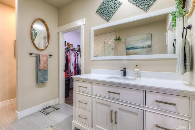 full bath featuring baseboards, walk in shower, a walk in closet, and vanity