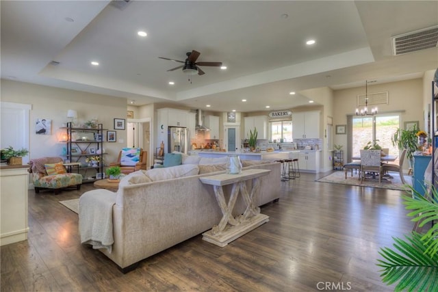 living room with visible vents, dark wood-style flooring, recessed lighting, a raised ceiling, and ceiling fan with notable chandelier