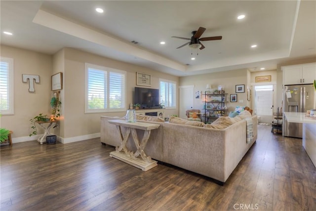 living area featuring ceiling fan, dark wood finished floors, baseboards, a tray ceiling, and visible vents