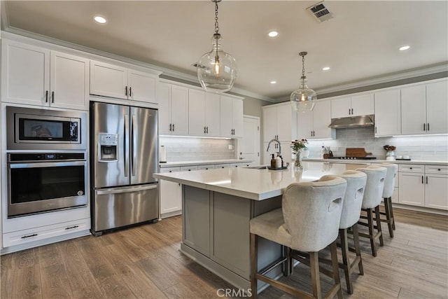 kitchen featuring visible vents, a sink, light countertops, under cabinet range hood, and stainless steel appliances