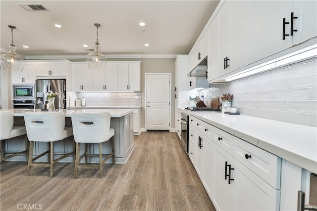 kitchen with a breakfast bar area, backsplash, crown molding, under cabinet range hood, and stainless steel appliances