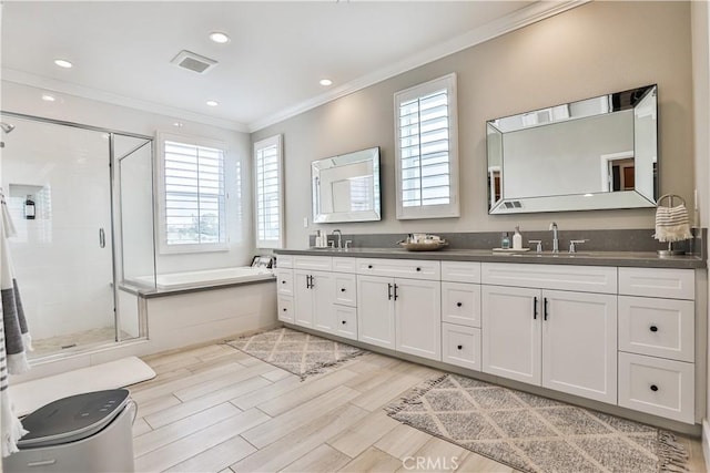 bathroom with a garden tub, double vanity, ornamental molding, a shower stall, and a sink