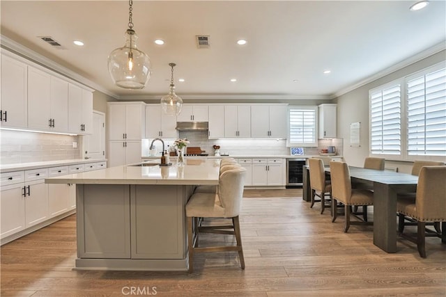 2454 Nova Way, Corona, CA 92883 - kitchen with a sink, ornamental molding, backsplash, light countertops, and an island with sink
