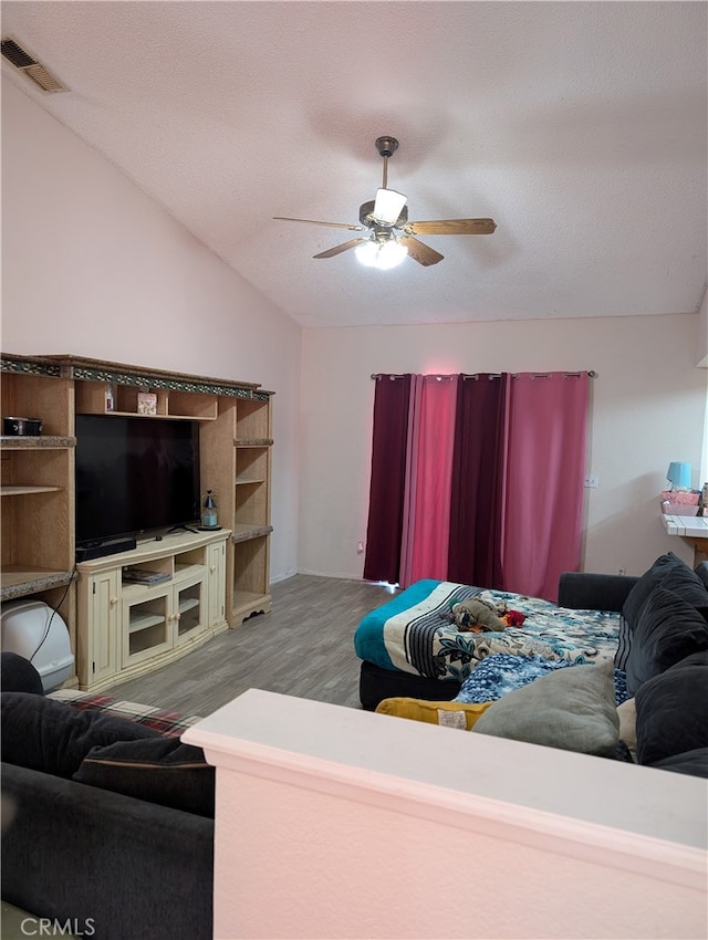 living area featuring wood finished floors, a textured ceiling, visible vents, ceiling fan, and vaulted ceiling