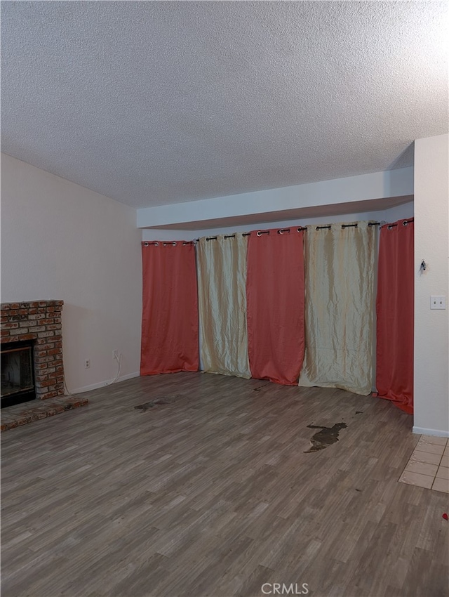 unfurnished living room featuring a textured ceiling, wood finished floors, baseboards, and a brick fireplace