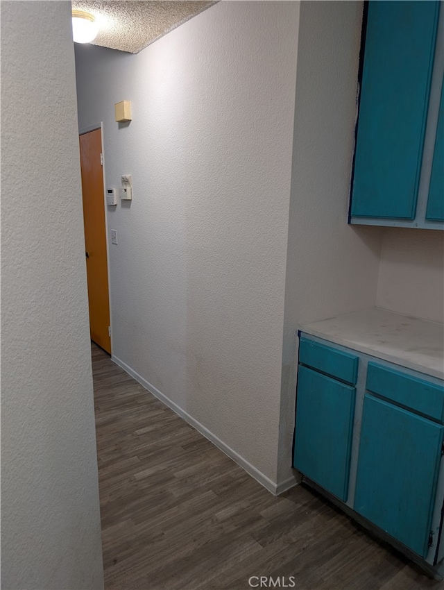 hallway with a textured ceiling, dark wood-style flooring, baseboards, and a textured wall