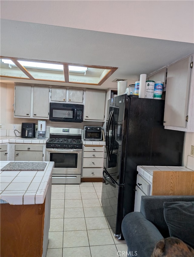 kitchen featuring a toaster, open floor plan, black appliances, tile countertops, and light tile patterned flooring