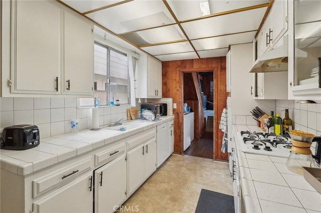 kitchen featuring tile counters, white dishwasher, under cabinet range hood, and wood walls