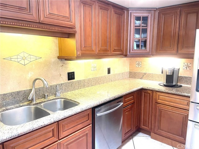 kitchen with a sink, dishwasher, light tile patterned floors, glass insert cabinets, and light stone countertops
