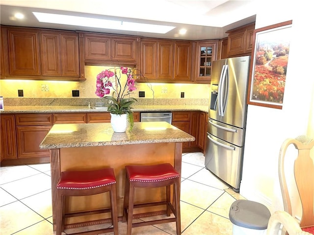 kitchen featuring glass insert cabinets, a kitchen bar, stainless steel appliances, a kitchen island, and light tile patterned flooring