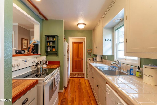 kitchen with white appliances, white cabinets, light wood finished floors, tile countertops, and a sink