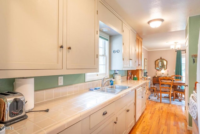 kitchen featuring ornamental molding, dishwasher, light wood finished floors, tile countertops, and a sink