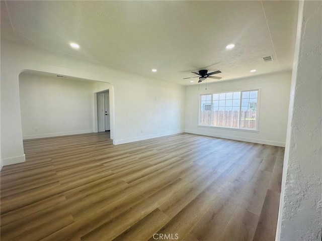 spare room featuring arched walkways, light wood-style floors, visible vents, and a ceiling fan