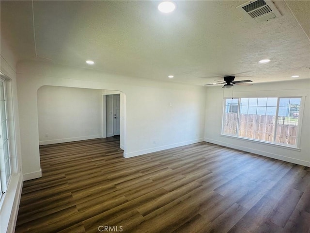 empty room with dark wood-style flooring, a textured ceiling, a ceiling fan, visible vents, and arched walkways
