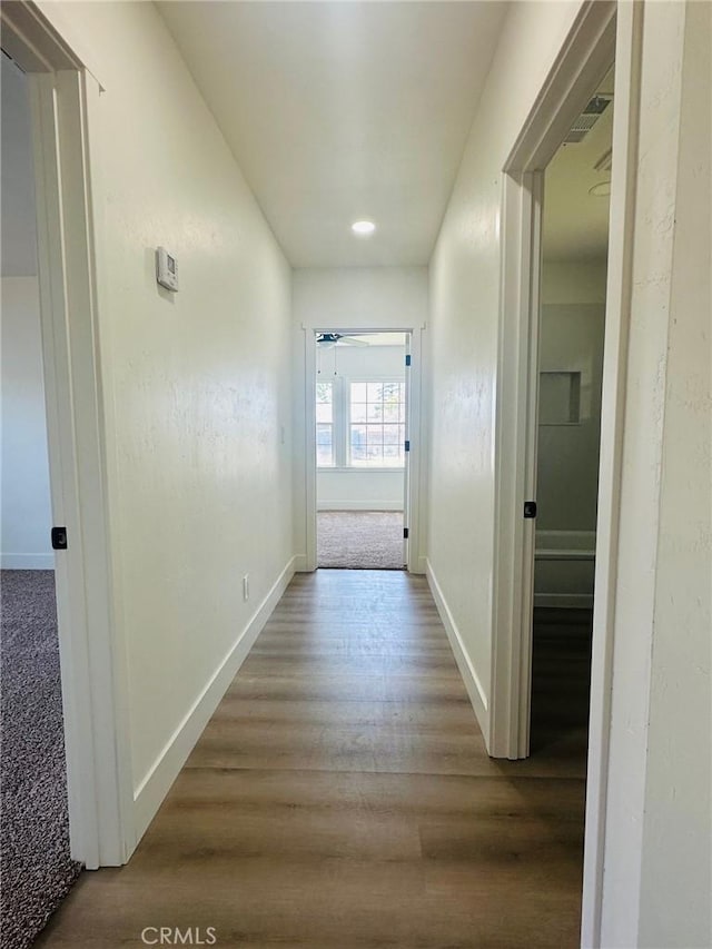hall with visible vents, baseboards, and wood finished floors