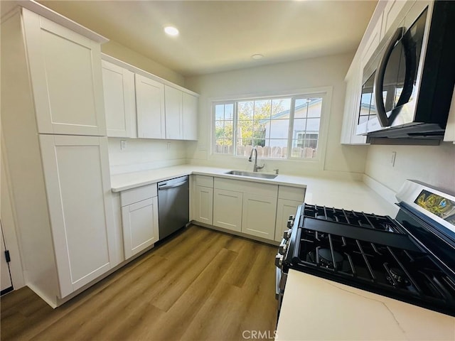 kitchen featuring appliances with stainless steel finishes, wood finished floors, a sink, and white cabinets