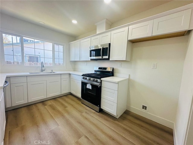 kitchen featuring appliances with stainless steel finishes, light wood finished floors, a sink, and baseboards