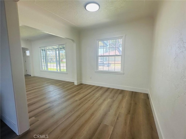 unfurnished room featuring a textured ceiling, wood finished floors, a textured wall, and baseboards