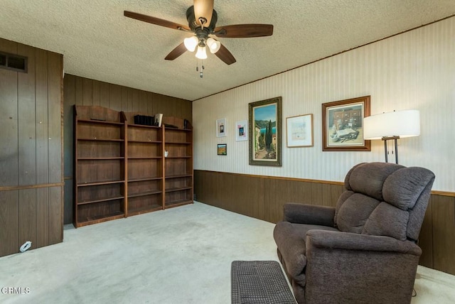 sitting room with carpet, a textured ceiling, a ceiling fan, visible vents, and wood walls