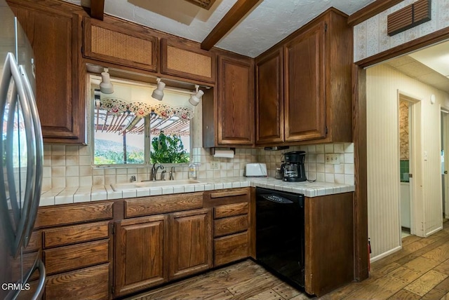 kitchen featuring tasteful backsplash, freestanding refrigerator, black dishwasher, light wood-style floors, and a sink