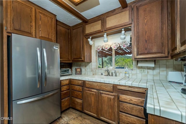 kitchen with glass insert cabinets, a sink, freestanding refrigerator, tile counters, and decorative backsplash