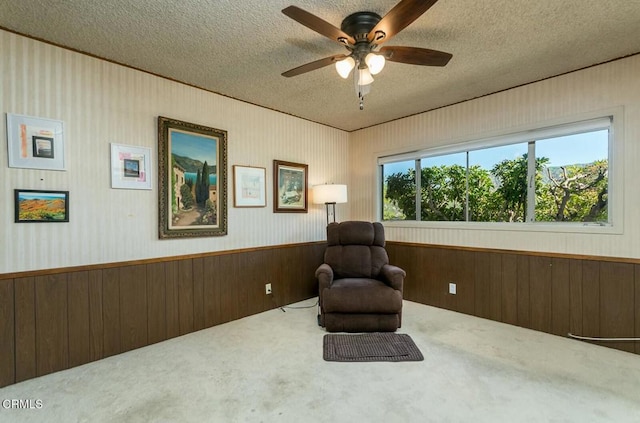 sitting room featuring ceiling fan, a textured ceiling, wood walls, carpet flooring, and wainscoting