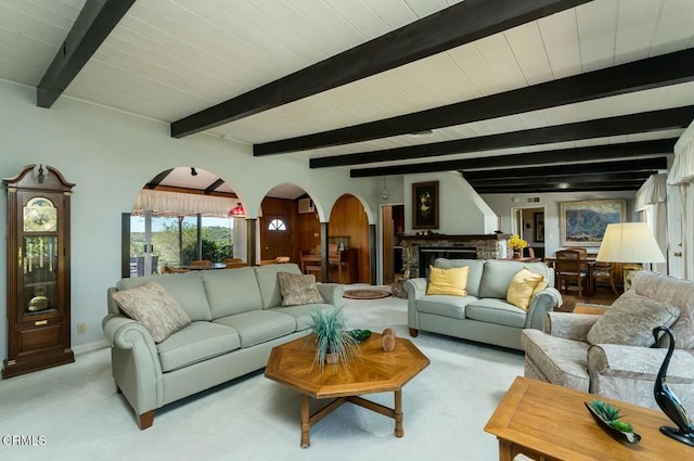 living area with arched walkways, light colored carpet, and beam ceiling