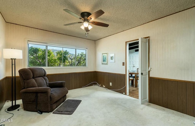 sitting room featuring wooden walls, carpet floors, a wainscoted wall, and a ceiling fan