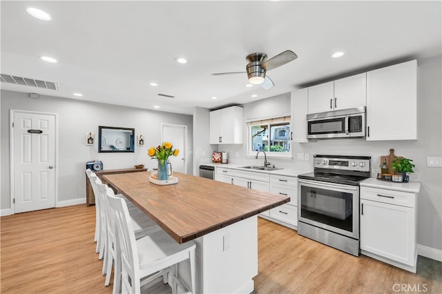 kitchen with stainless steel appliances, a sink, light wood-style flooring, butcher block counters, and recessed lighting