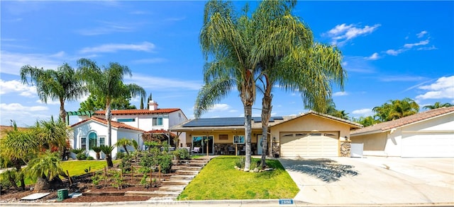 view of front of home with an attached garage, roof mounted solar panels, concrete driveway, stucco siding, and a front lawn