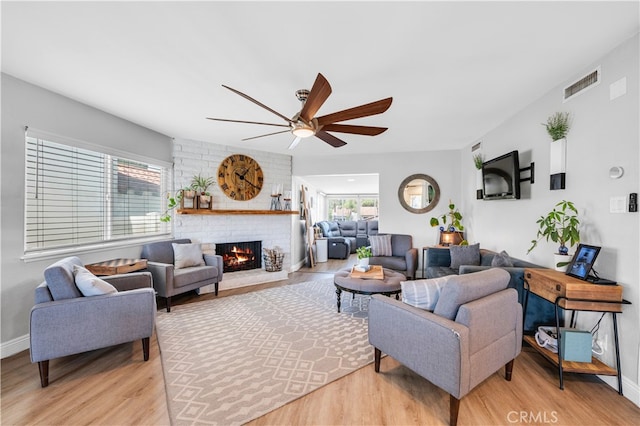 living room with light wood-style floors, a ceiling fan, a fireplace, and healthy amount of natural light