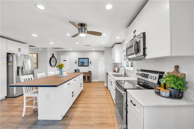 kitchen featuring stainless steel appliances, a sink, a kitchen breakfast bar, a kitchen island, and ceiling fan
