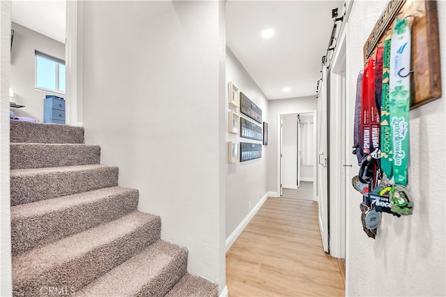 corridor with a barn door, light wood finished floors, stairs, baseboards, and recessed lighting