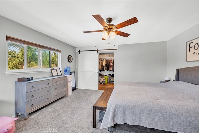 bedroom featuring a barn door, carpet floors, ceiling fan, and a closet
