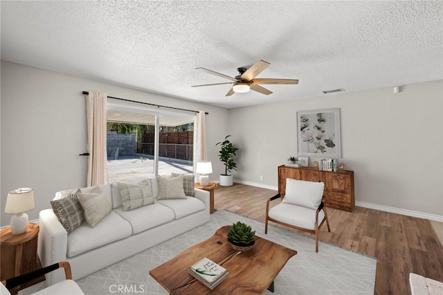 living area featuring visible vents, baseboards, a ceiling fan, and wood finished floors