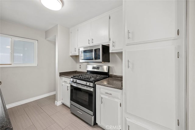 kitchen with stainless steel appliances, white cabinetry, baseboards, and dark countertops