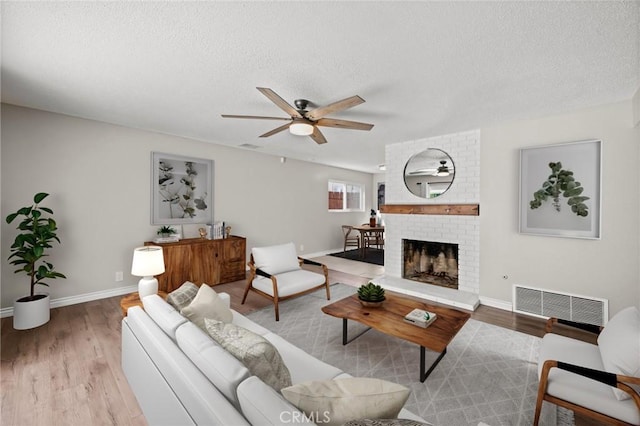 living area with wood finished floors, ceiling fan, a brick fireplace, and visible vents
