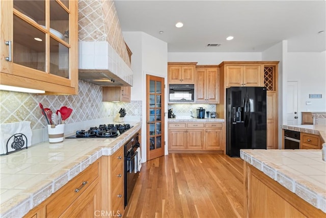 29083 Mammoth Dr, Lake Arrowhead, CA 92352 - kitchen with black appliances, light wood-style flooring, tile counters, glass insert cabinets, and custom range hood