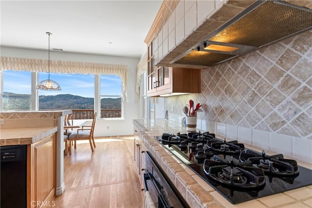 29083 Mammoth Dr, Lake Arrowhead, CA 92352 - kitchen with tile countertops, premium range hood, black appliances, light wood-style flooring, and decorative backsplash