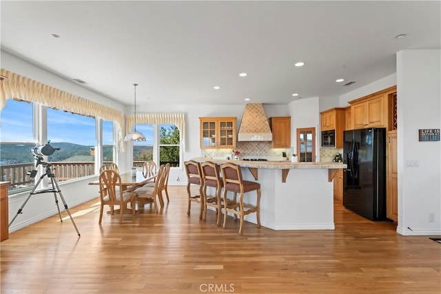 29083 Mammoth Dr, Lake Arrowhead, CA 92352 - kitchen with black fridge, custom exhaust hood, light countertops, a kitchen bar, and decorative backsplash