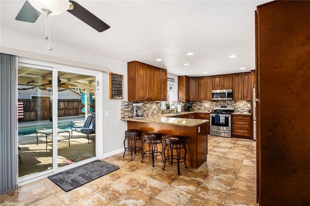 kitchen featuring a ceiling fan, decorative backsplash, a peninsula, appliances with stainless steel finishes, and light stone countertops