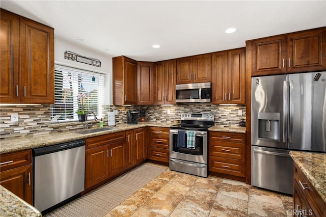 kitchen featuring light stone countertops, decorative backsplash, stainless steel appliances, and a sink