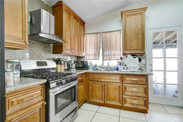 kitchen with tasteful backsplash, brown cabinets, wall chimney exhaust hood, and stainless steel range with gas cooktop