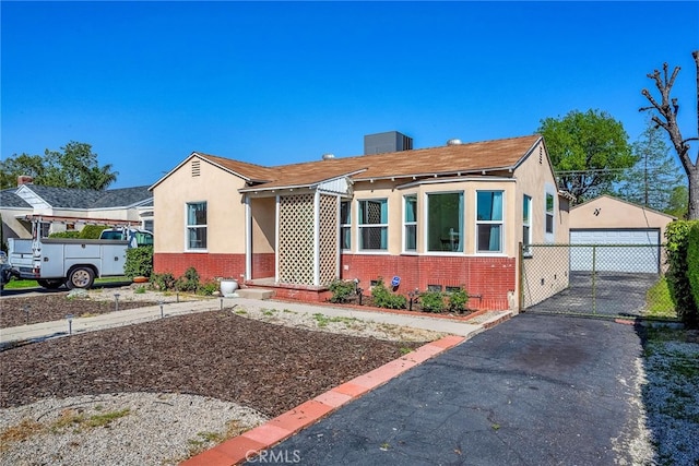 bungalow-style home with a garage, brick siding, stucco siding, and an outbuilding