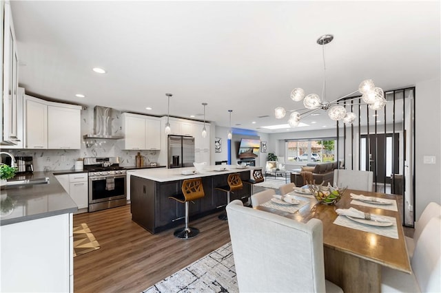 kitchen with wall chimney range hood, white cabinets, appliances with stainless steel finishes, a sink, and wood finished floors