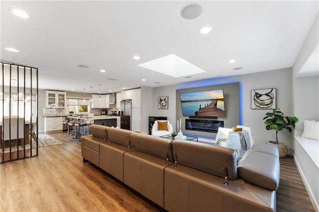living area featuring a skylight, baseboards, recessed lighting, and light wood-style flooring