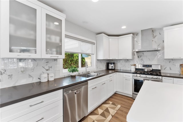 kitchen featuring dark countertops, wall chimney range hood, a sink, appliances with stainless steel finishes, and backsplash