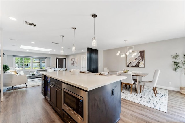 kitchen featuring visible vents, light wood-style floors, open floor plan, light countertops, and stainless steel microwave