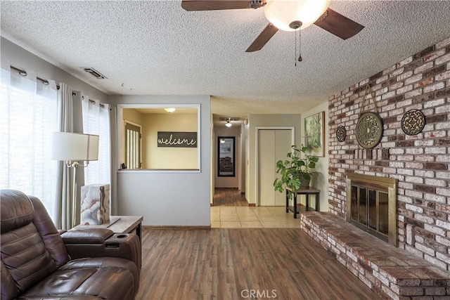 living area featuring ceiling fan, a textured ceiling, visible vents, and a fireplace